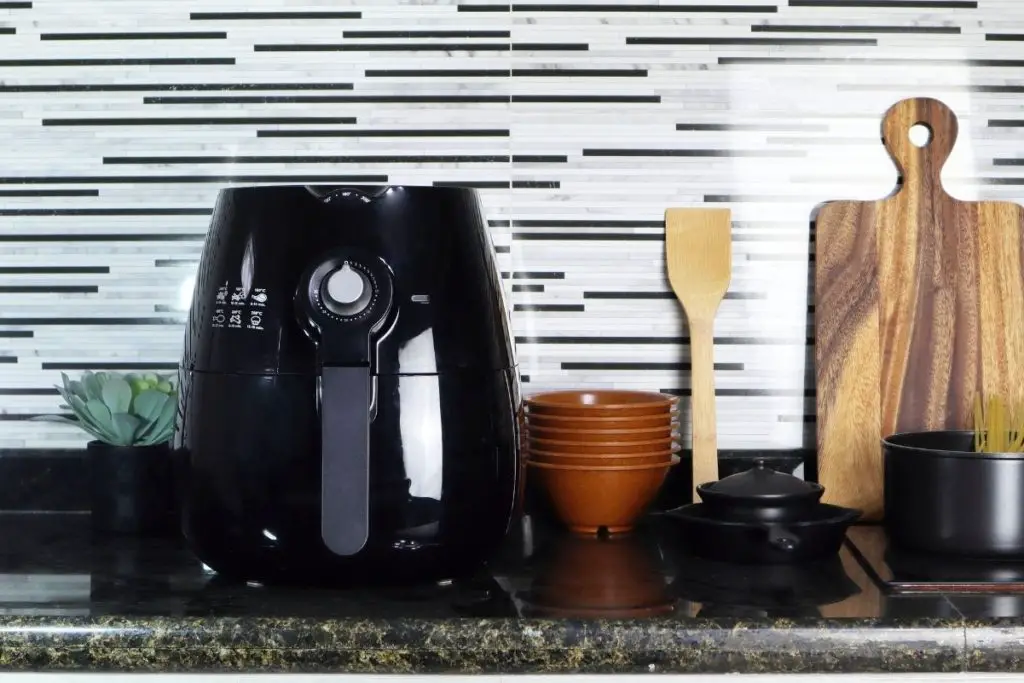 A black air fryer on a kitchen counter next to kitchen utensils.