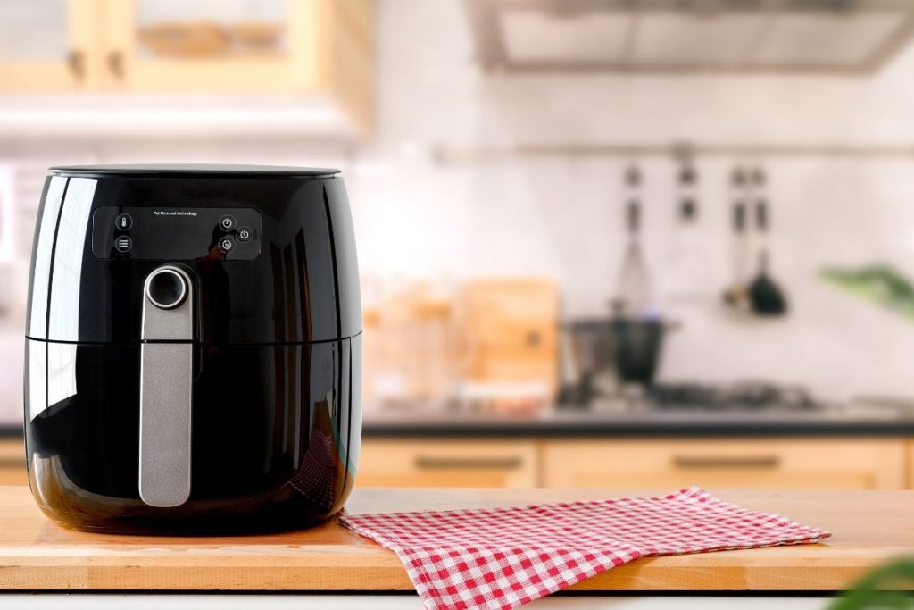 A black air fryer on a counter with a red and white napkin next to it. An out of focus background.