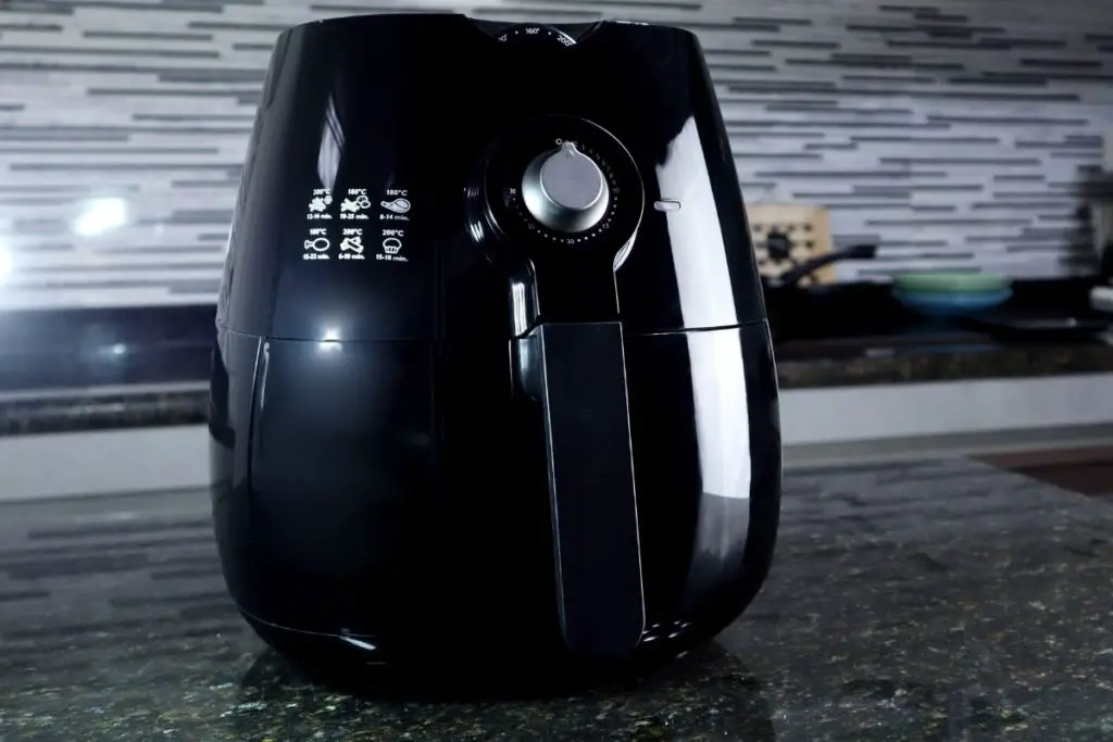 A black air fryer on a dark counter, with an out of focus background.