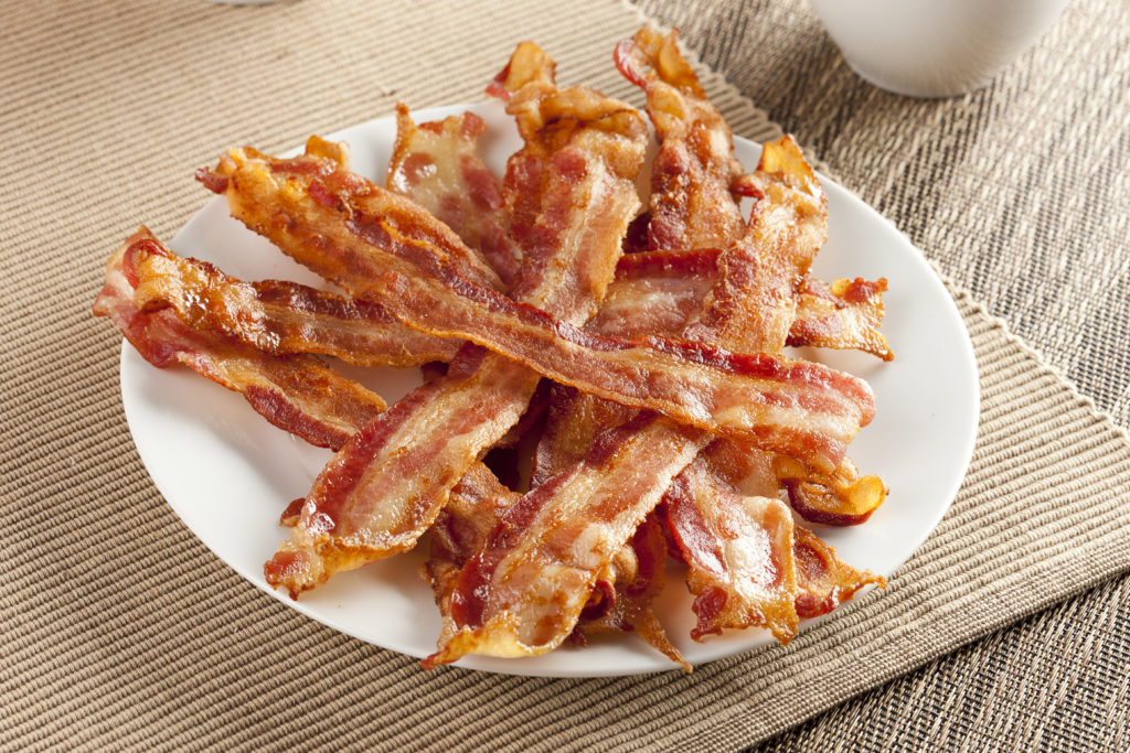 A pile of cooked bacon on a white plate sitting on a tan placemat.