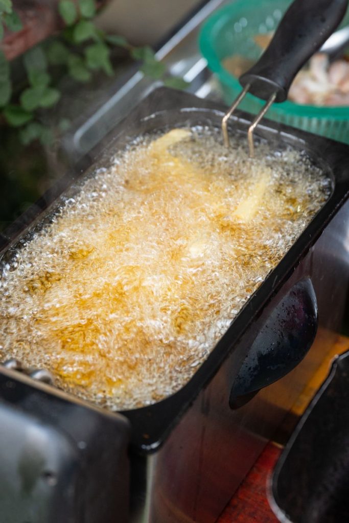 A rectangular deep fryer with boiling oil and French Fries.