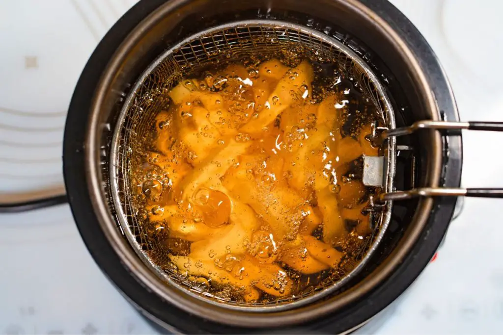 Closeup of a deep fryer full of hot oil and french fries.