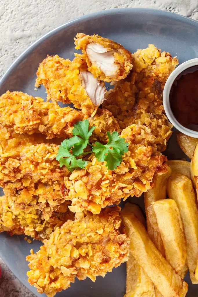 Fried chicken and french fries on a dark plate, on a gray surface.