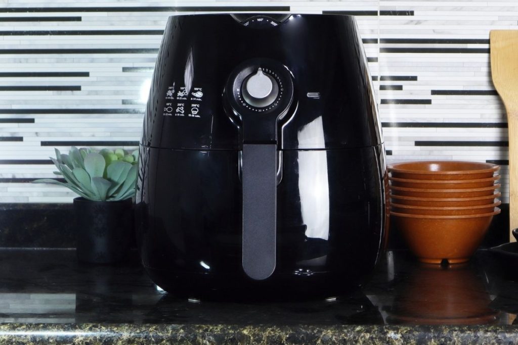 A black air fryer on a kitchen counter with cooking tools next to it.
