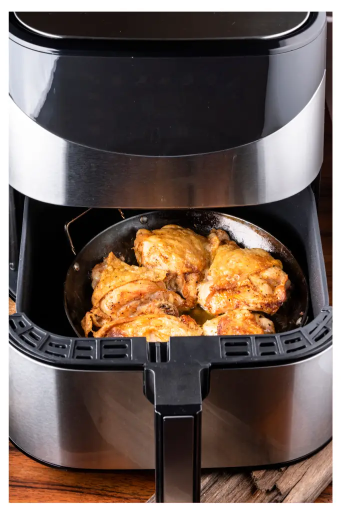 A black air fryer with the basket open and filled with fried chicken.