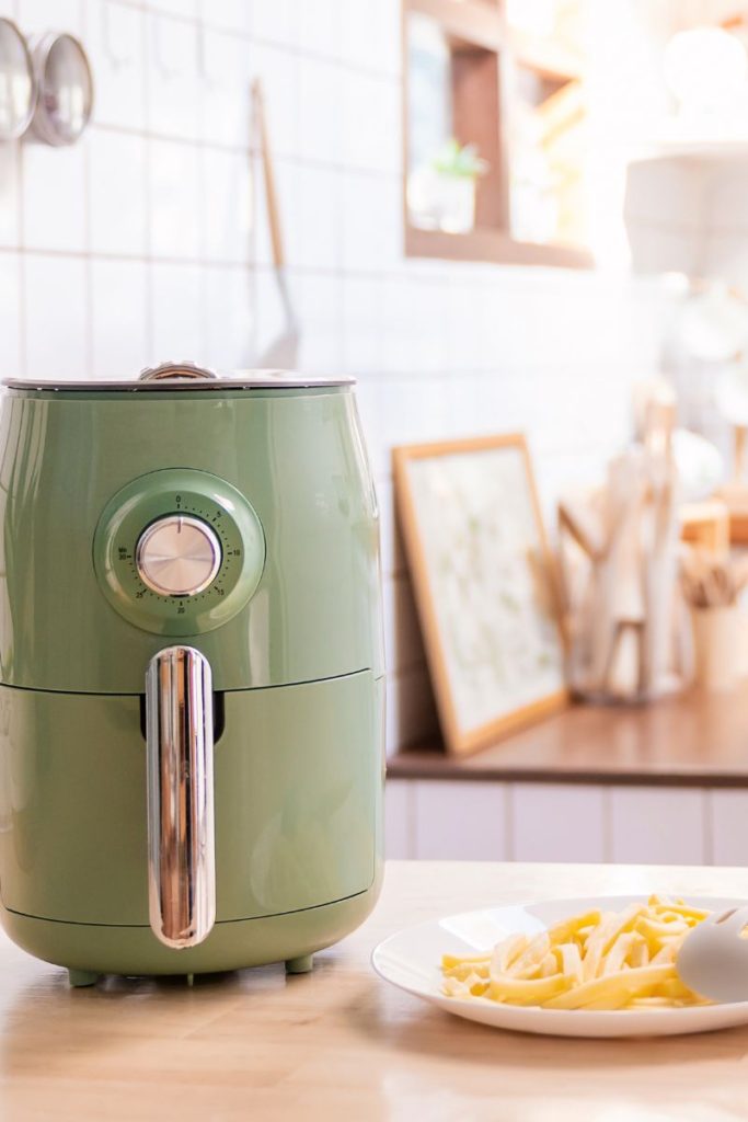 A Green air fryer on a kitchen counter with a plate of french fries next to it.