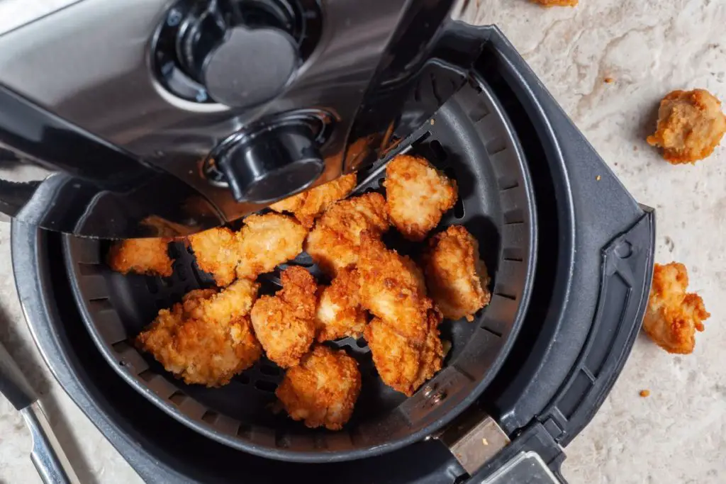 An overhead view of an air fryer with the basket open and filled with cooked nuggets.