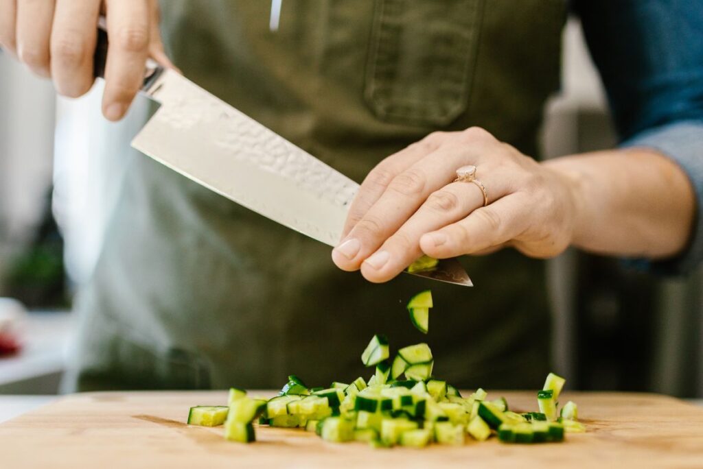 Hands cutting vegetables with a chef's knife.