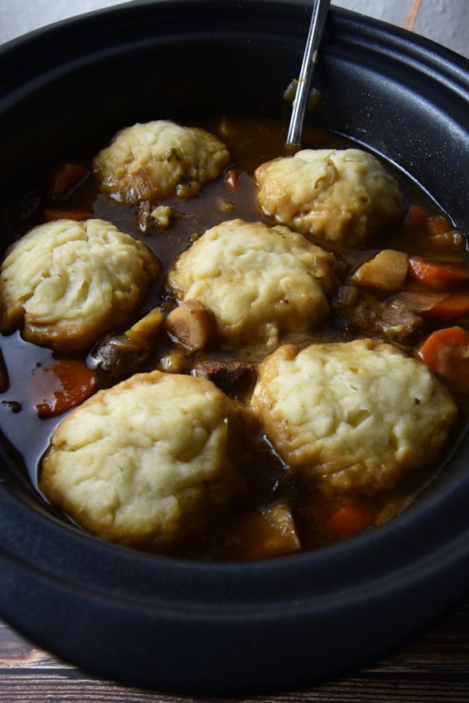 A black slow cooker with a red stew topped with biscuits.