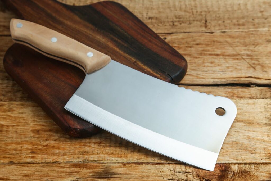 A Western cleaver on a dark wooden cutting board, that is sitting a a light wooden surface.