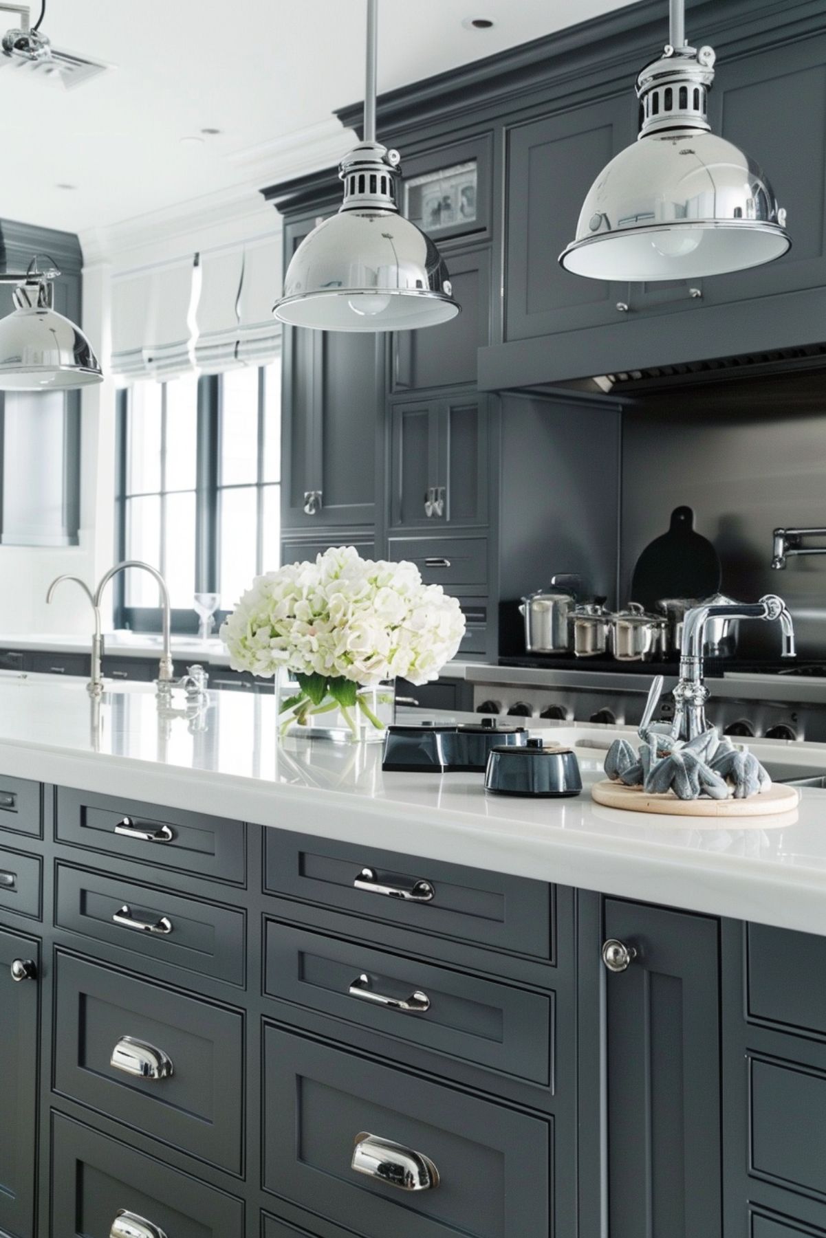 Contemporary kitchen with dark gray cabinetry, white countertops, and stainless steel accents. The kitchen features industrial-style pendant lights, a large central island with a sink, and a bouquet of white flowers, creating a modern and stylish space.