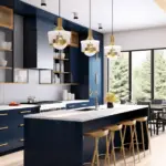 modern kitchen with a strong design aesthetic featuring deep indigo cabinetry and gold accents. The kitchen includes an island with a white countertop and indigo base, surrounded by minimalist wooden bar stools. Above the island hang elegant white and gold pendant lights, adding a luxurious touch. The cabinetry, with gold handles, is mixed with sections of open shelving that display neatly organized kitchen essentials. The space is bright, with a large window offering a view of a wooded area, and it seamlessly integrates into an open dining area in the background.