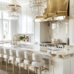 A luxury white kitchen with gold accents, and 2 crystal chandeliers.