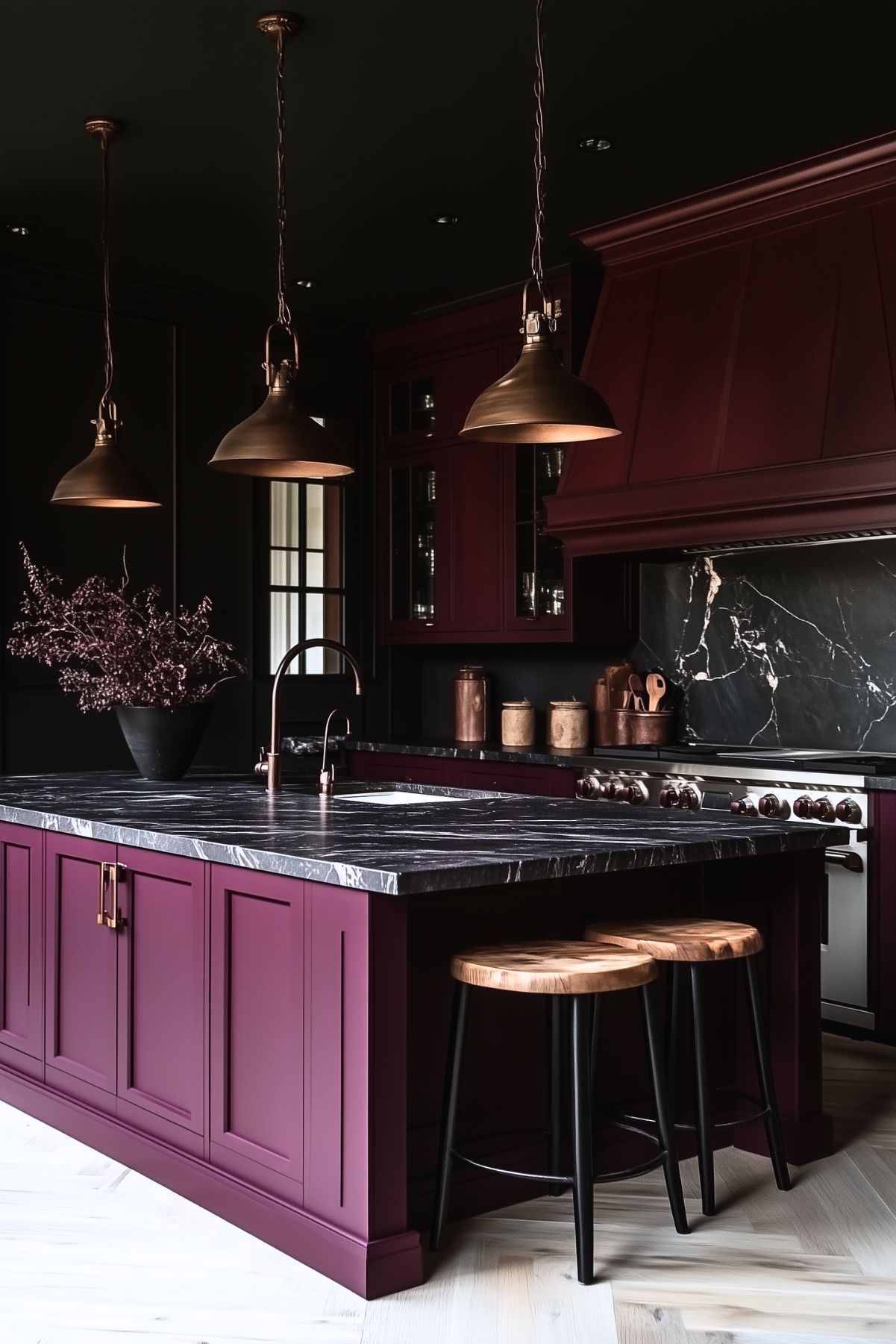 Bold kitchen design with rich burgundy cabinetry and a striking black marble countertop and backsplash. The dark, dramatic palette is complemented by brass pendant lights and hardware. Wooden barstools with black metal legs add warmth and texture, while sleek copper accents and minimalist decor complete the modern yet luxurious space.