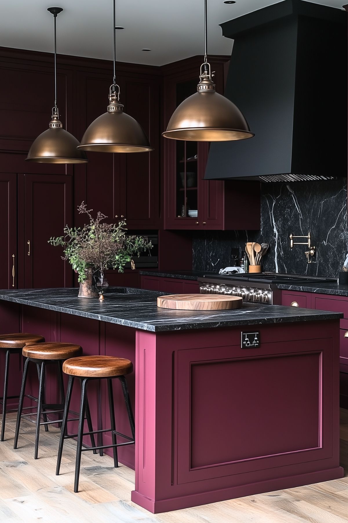 Chic modern kitchen with deep burgundy cabinetry and a matching island. The black marble countertops and backsplash provide a dramatic contrast, complemented by bronze pendant lights hanging above the island. Wooden stools add a rustic touch, while sleek appliances and minimalist decor complete the sophisticated design.