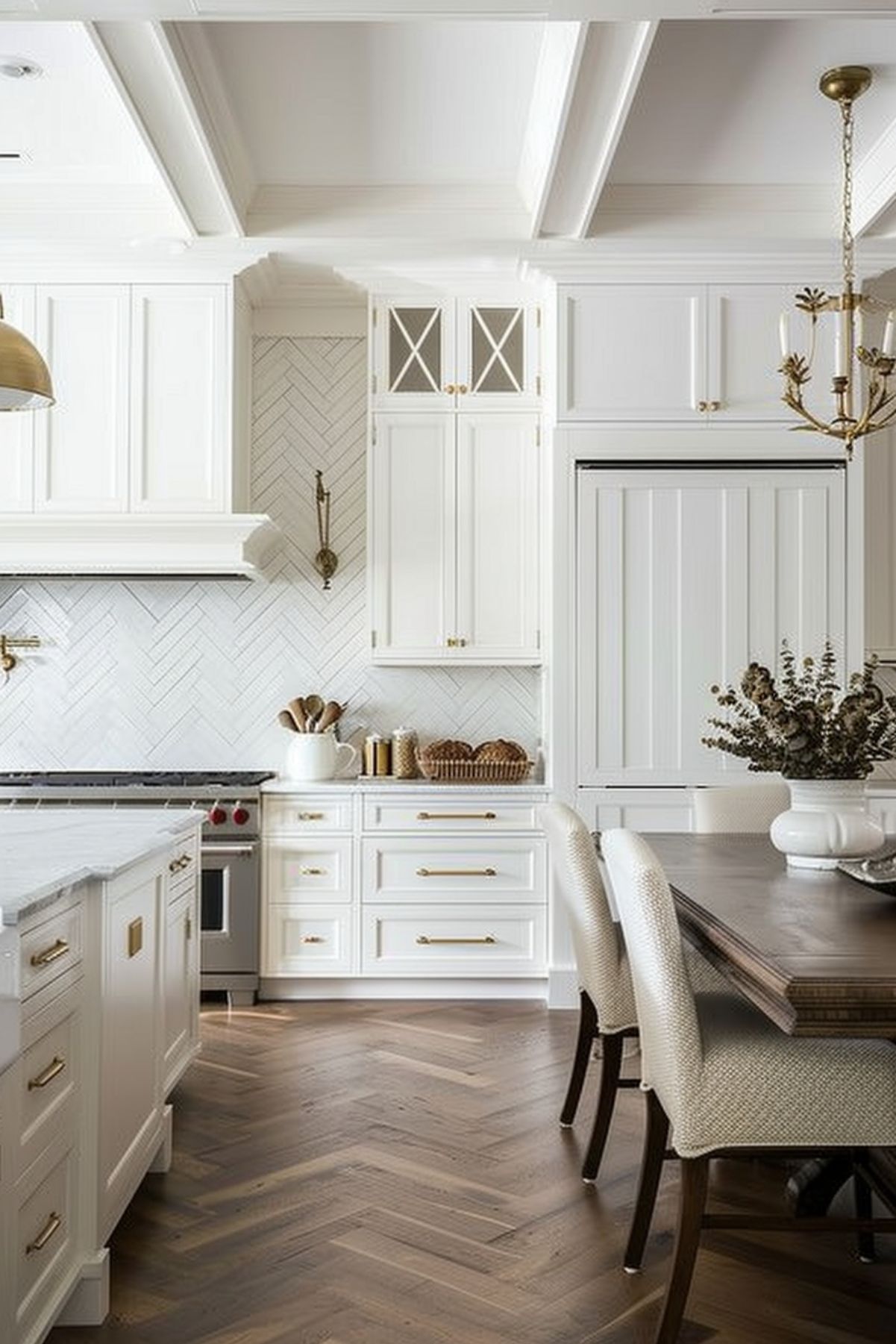 An elegant kitchen design that combines classic and contemporary elements. The space features white cabinetry with gold hardware, herringbone backsplash, and a marble countertop. A rustic wooden dining table paired with upholstered chairs sits under a vintage chandelier, complemented by coffered ceilings and warm wooden floors, creating a welcoming and sophisticated atmosphere.