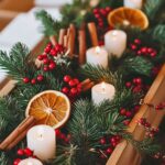 Natural holiday centerpiece with evergreen branches, red berries, cinnamon sticks, dried orange slices, and small white candles, creating a warm and festive look.