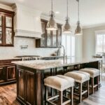 Dark wood kitchen island with upholstered stools, marble countertop, pendant lighting, and matching dark cabinetry in a spacious kitchen.