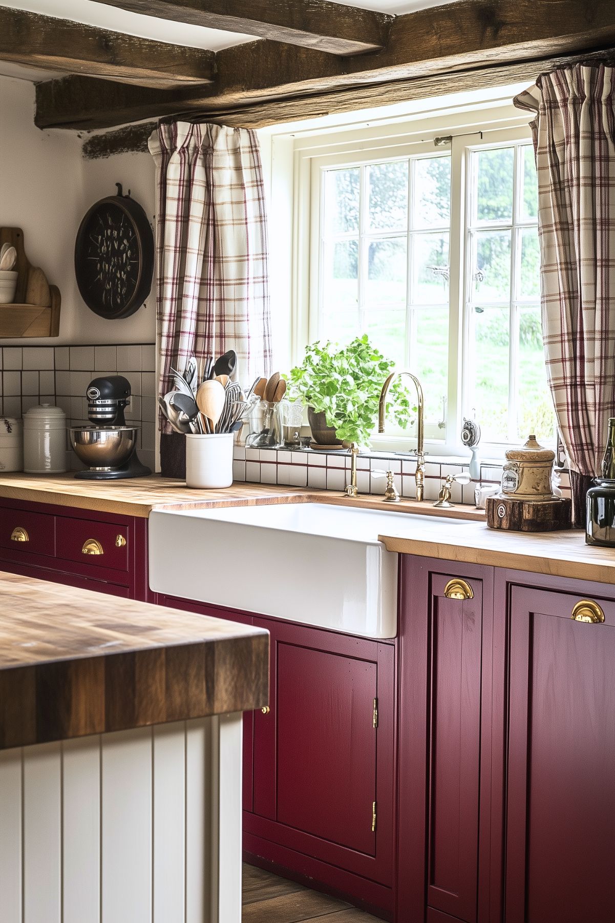 Rustic kitchen with burgundy lower cabinets, butcher block countertops, farmhouse sink, plaid curtains, and exposed wooden ceiling beams. The countertop is decorated with a potted plant, utensils in a ceramic holder, and vintage-style decor, enhancing the cozy farmhouse vibe.