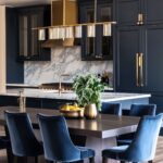 Elegant kitchen with navy cabinets, gold hardware, marble backsplash, velvet dining chairs, and a modern gold chandelier for a luxurious feel.