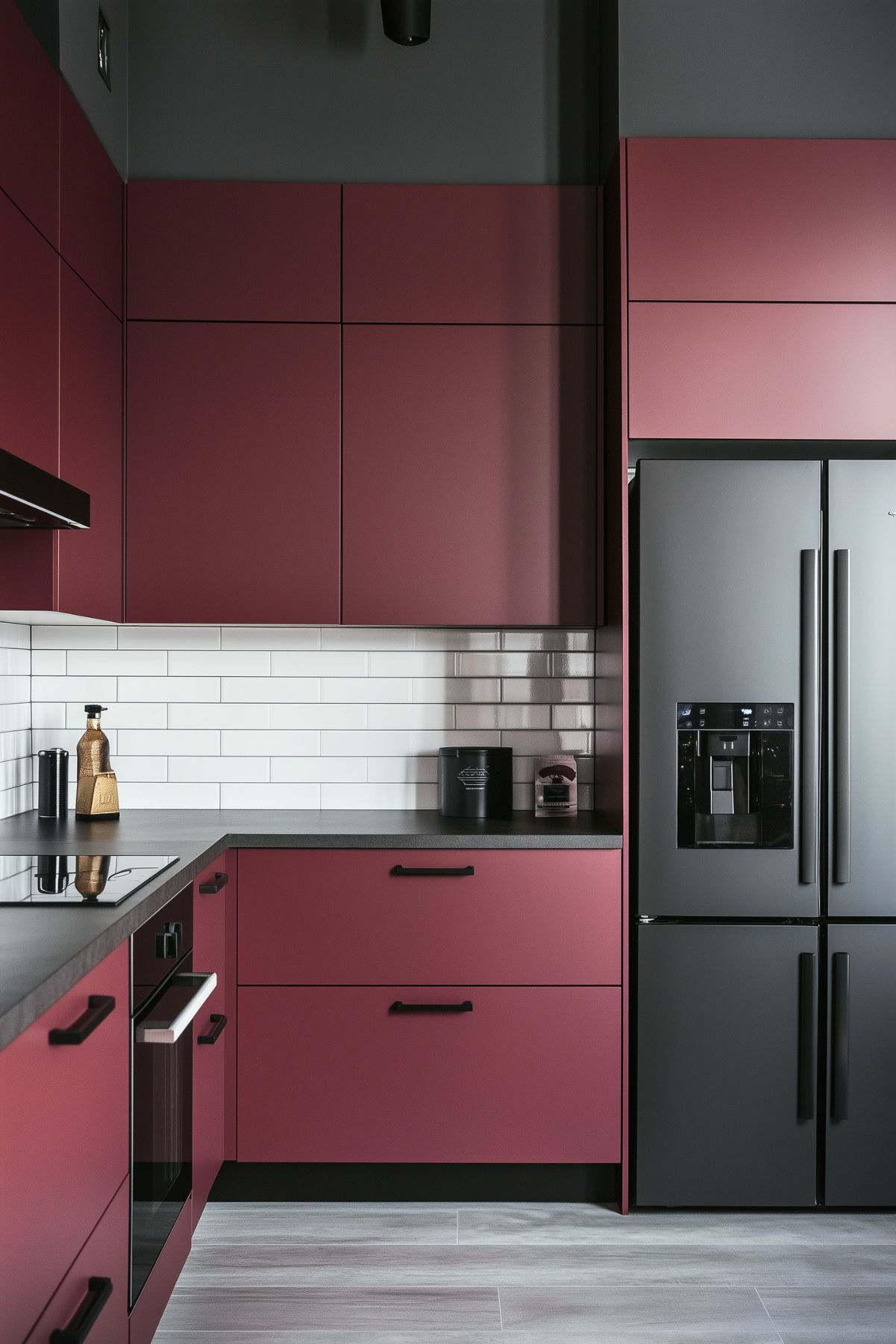 Minimalist kitchen with matte burgundy cabinets, black countertops, and a black refrigerator. The backsplash features white subway tiles, and the design incorporates black handles and accents, creating a sleek, modern look with a balanced contrast of dark and light elements.