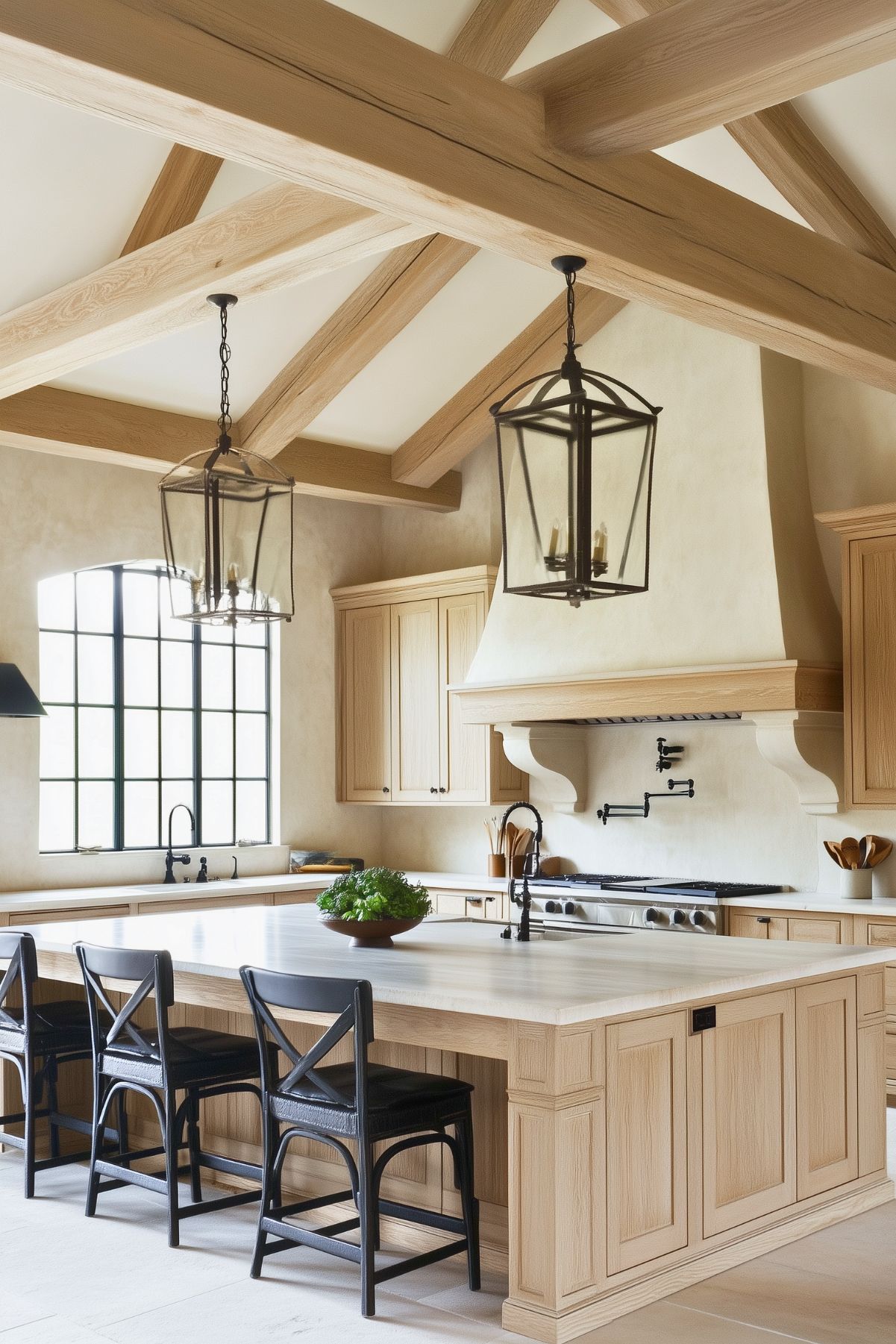 Rustic kitchen with white oak cabinetry, large center island, black cross-back bar stools, exposed wooden ceiling beams, lantern pendant lighting, and plaster range hood, complemented by a farmhouse-style sink and matte black fixtures.