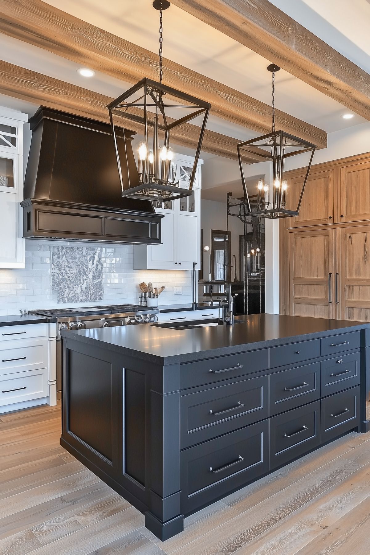 Stylish kitchen with a striking contrast of dark grey island cabinetry against light oak wood beams and white walls. Features include elegant geometric chandeliers, stainless steel appliances, and a white subway tile backsplash, providing a modern yet classic look."