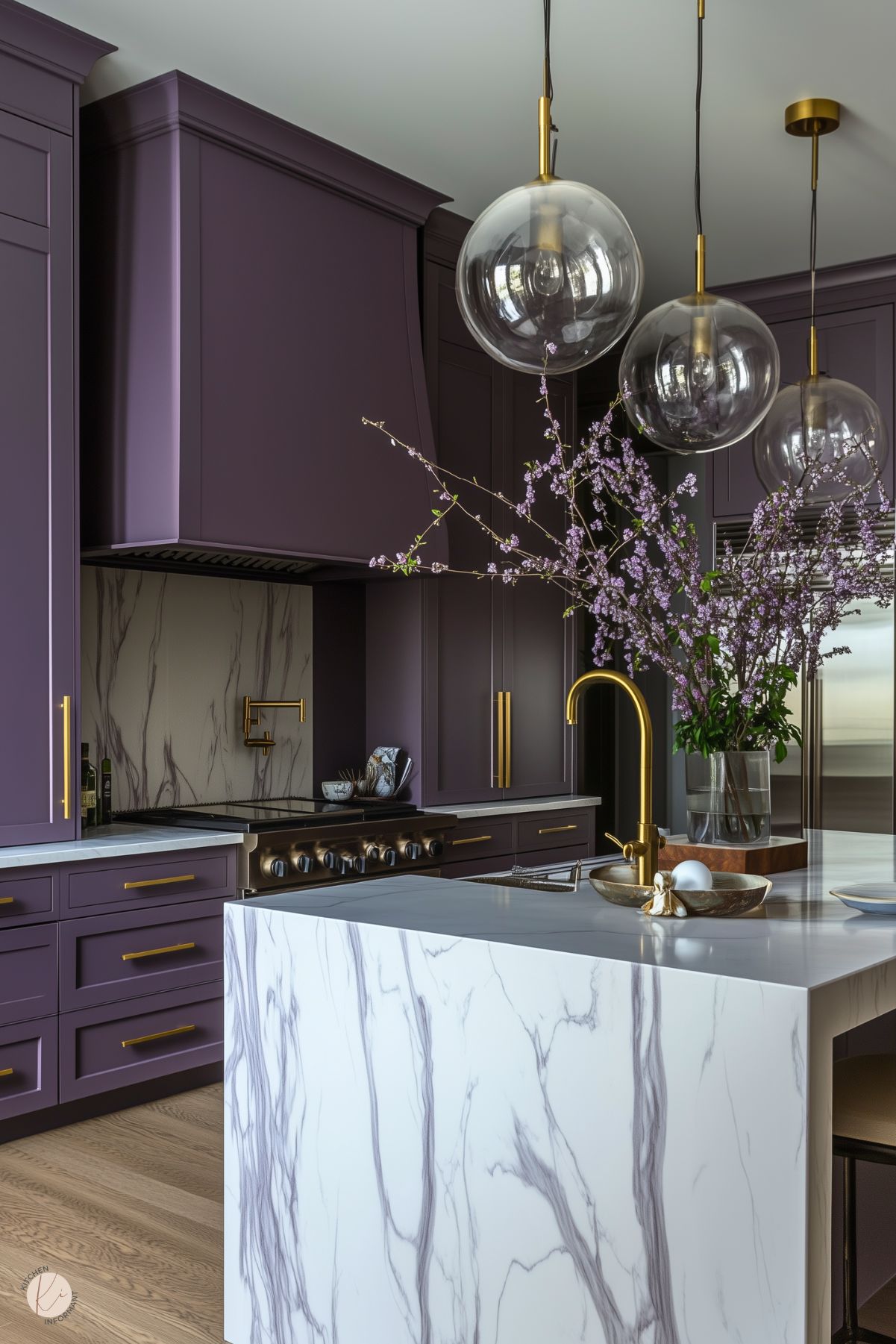 Sophisticated kitchen with deep plum cabinetry, gold hardware, and a dramatic marble backsplash and waterfall island. The design is enhanced by modern globe pendant lights and a vase of blossoming branches, adding a luxurious and elegant touch.