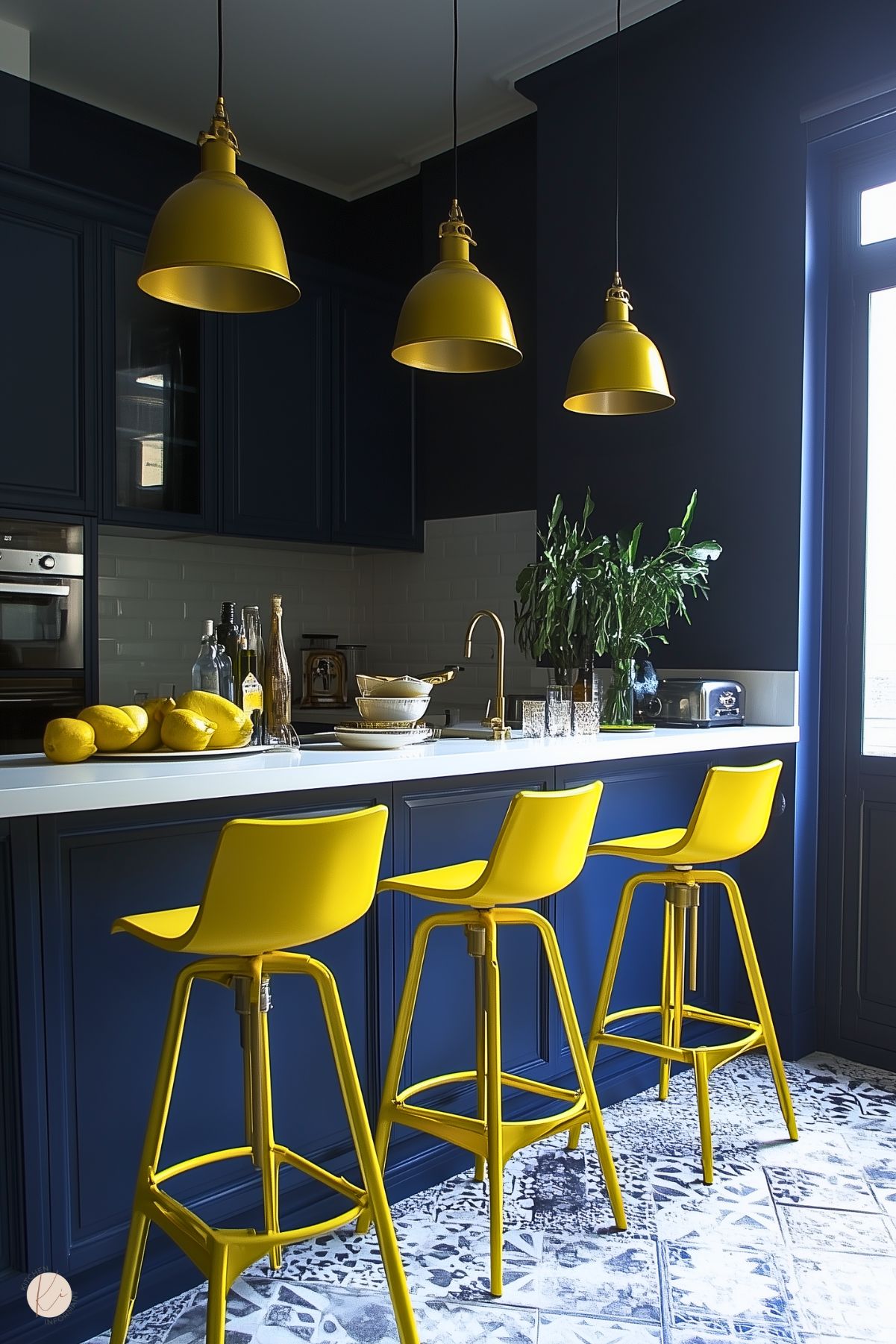 Modern navy blue kitchen with bold yellow bar stools and pendant lights. The design features a white countertop, gold faucet accents, and patterned floor tiles, creating a striking contrast with vibrant pops of color.