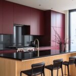 Modern kitchen featuring deep burgundy cabinets, a black countertop, natural wood accents, and sleek bar seating for a stylish and functional design.