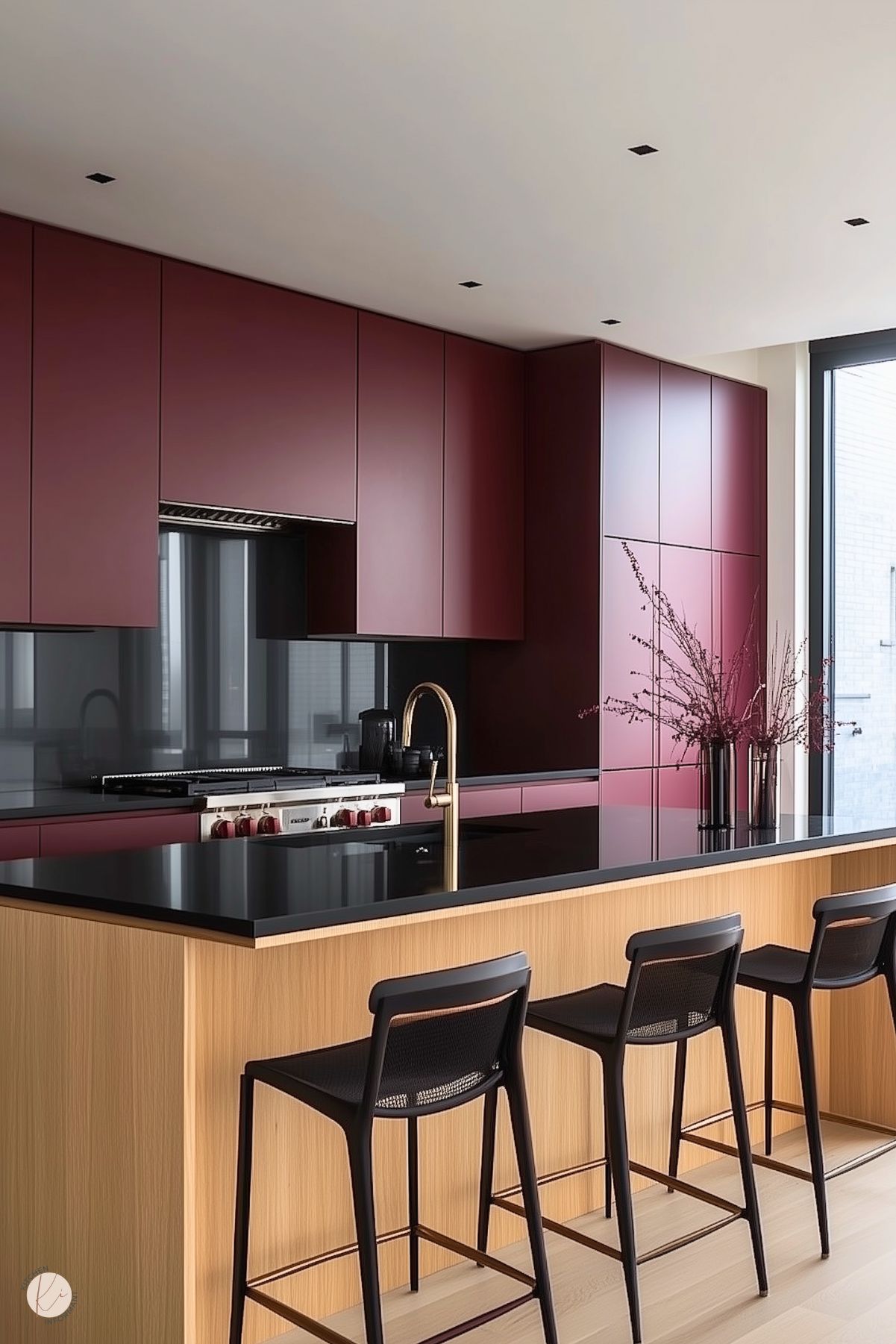 Modern kitchen featuring deep burgundy cabinets, a black countertop, natural wood accents, and sleek bar seating for a stylish and functional design.