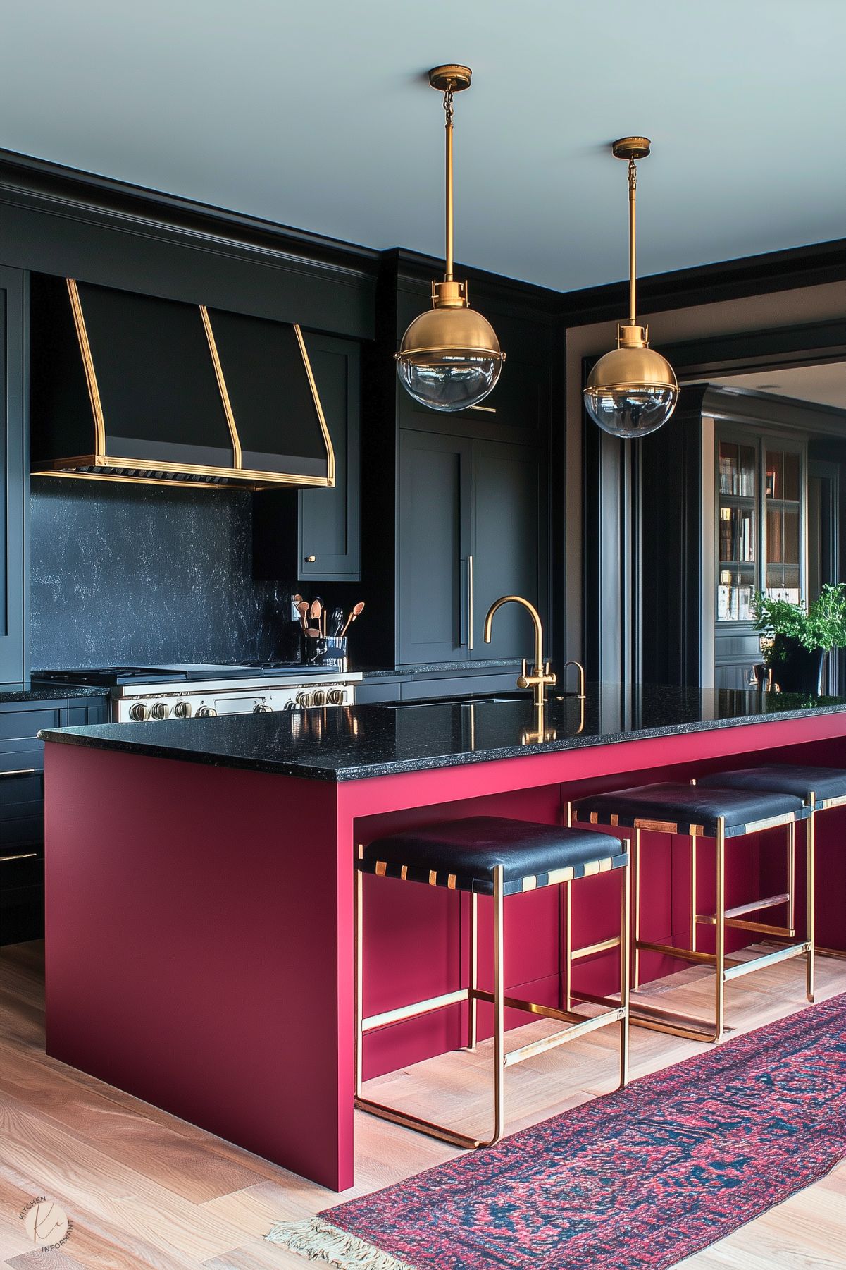 A sleek and modern kitchen featuring a bold burgundy island with a black stone countertop. The island is paired with gold-accented stools and pendant lights with glass globes, creating a luxurious ambiance. The black cabinetry and range hood with gold trim enhance the dramatic design. A red patterned rug adds warmth, while light wood flooring balances the dark and vibrant tones of the space.