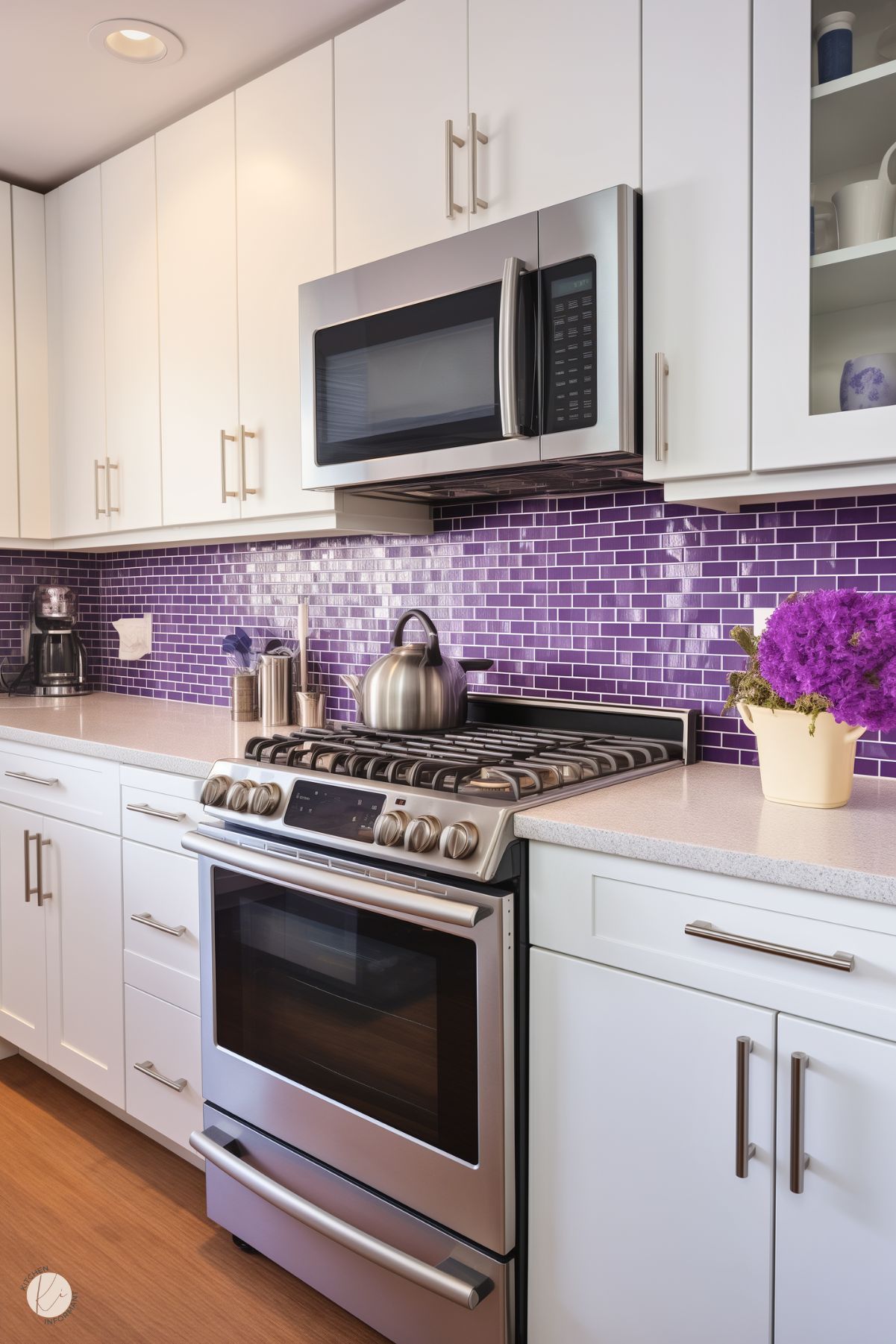 A modern kitchen with white cabinetry, sleek stainless steel appliances, and a vibrant purple subway tile backsplash. The countertop features a stainless steel kettle, a coffee maker, and a pot of bright purple flowers, adding a lively pop of color to the clean, contemporary design.