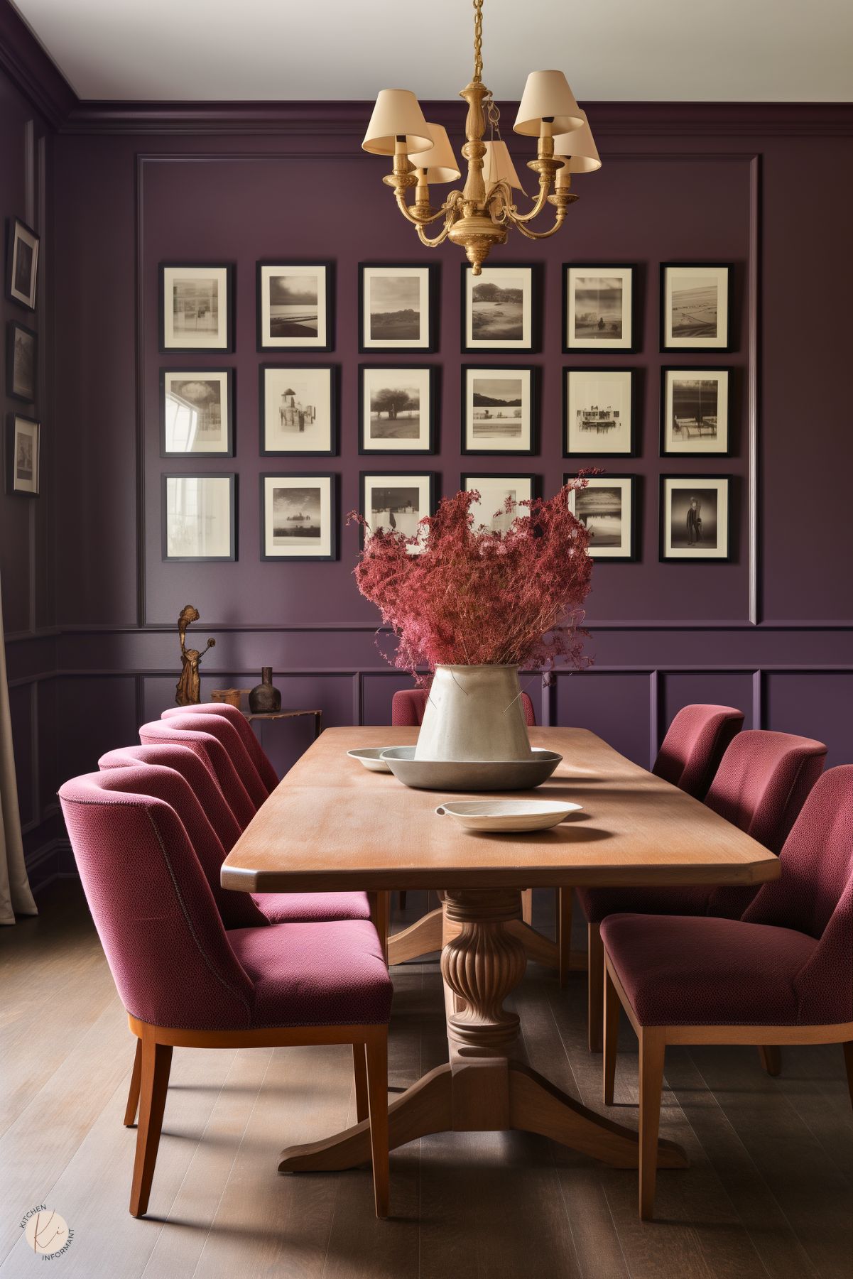 A dark academia dining room with plum-colored walls, a wooden table, and upholstered burgundy chairs. A gold chandelier adds warmth, while a gallery wall of black-and-white framed photographs enhances the scholarly aesthetic. A centerpiece of dried florals in a rustic vase completes the refined, moody atmosphere.