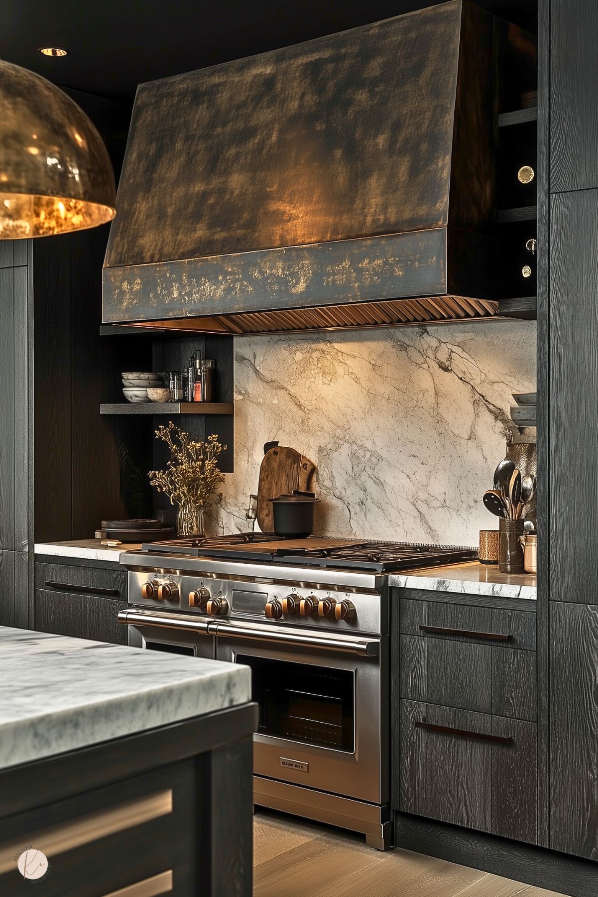 A luxurious kitchen with dark wood cabinetry and a bold marble backsplash and countertop. The centerpiece is a high-end stainless steel range with brass knobs, complemented by a large, textured metallic range hood with a patina finish. Open shelving displays elegant bowls and spices, adding a functional yet decorative touch. A vase of dried flowers and warm accent lighting enhance the sophisticated, rustic-modern ambiance, while light wood flooring provides subtle contrast.