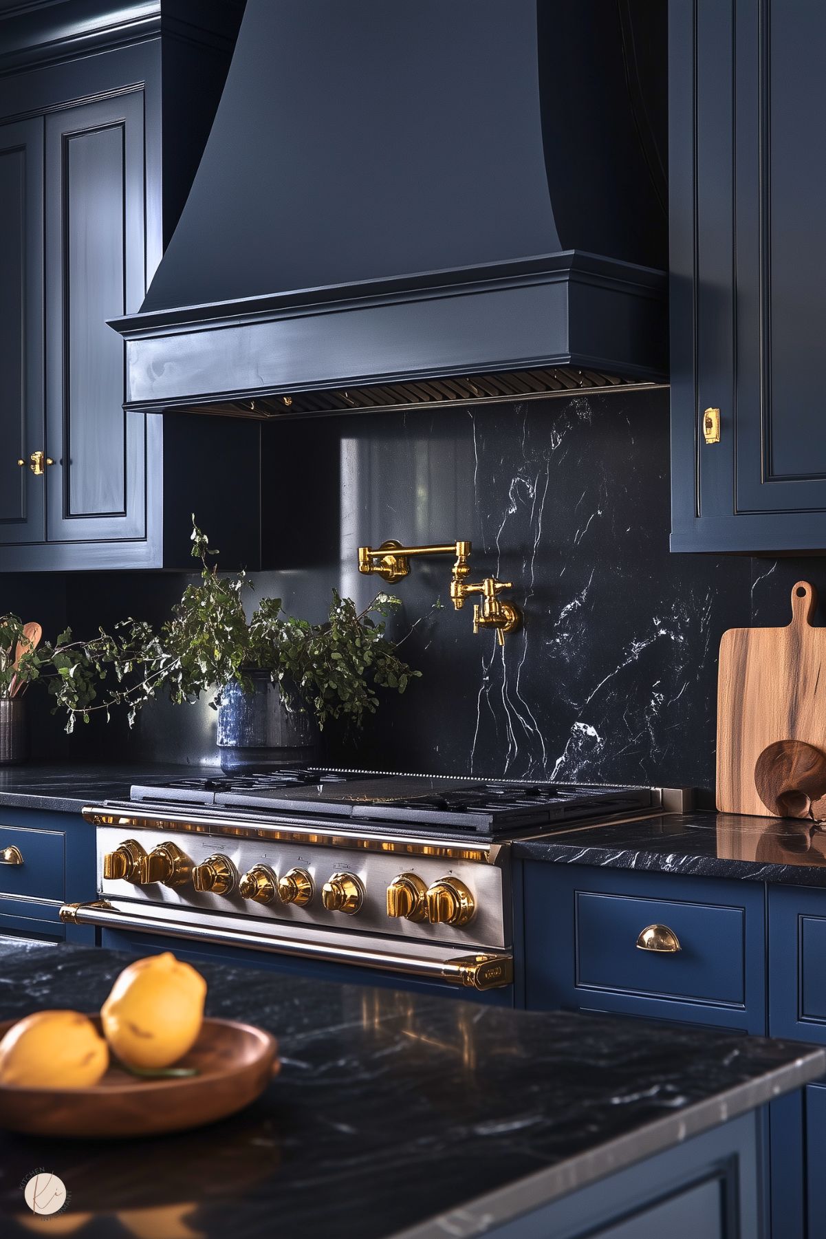 A sophisticated kitchen with deep navy cabinetry and a large range hood, complemented by a black marble backsplash with elegant white veining. The centerpiece is a stainless steel range adorned with gold knobs and accents, paired with a matching gold pot filler. The countertops feature the same luxurious black marble, while natural wood cutting boards and a bowl of bright yellow lemons add warmth and contrast. Decorative greenery enhances the stylish, upscale ambiance.