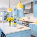 A vibrant kitchen with pastel blue cabinetry and a white countertop island. Yellow pendant lights add a cheerful contrast, complementing the vase of yellow flowers and a bowl of lemons on the island. The backsplash features white subway tiles, and stainless steel appliances, including a range hood and oven, provide a modern touch. Large windows in the background bring in natural light, enhancing the bright and welcoming atmosphere.