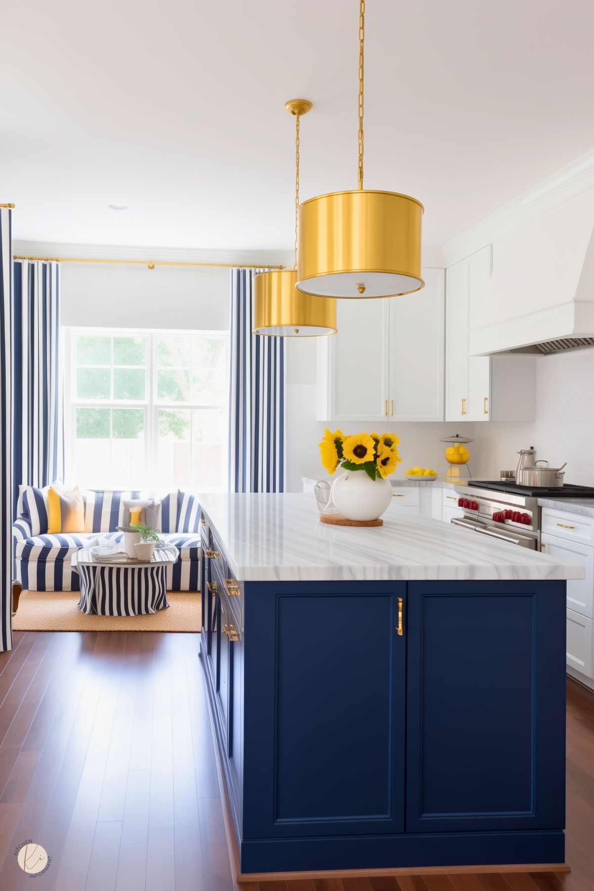 A bright preppy kitchen with a navy blue island, marble countertop, gold pendant lights, striped navy and white curtains, and matching striped seating adorned with yellow accents and sunflowers.