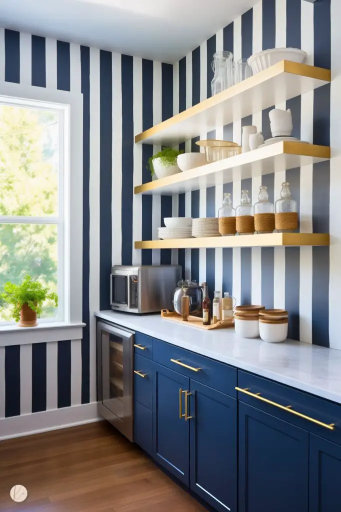 A playful preppy kitchen nook featuring navy and white striped walls, navy cabinetry with gold hardware, and open gold shelving. The space is accented with marble countertops, glass jars, and fresh greenery for a clean and vibrant look.