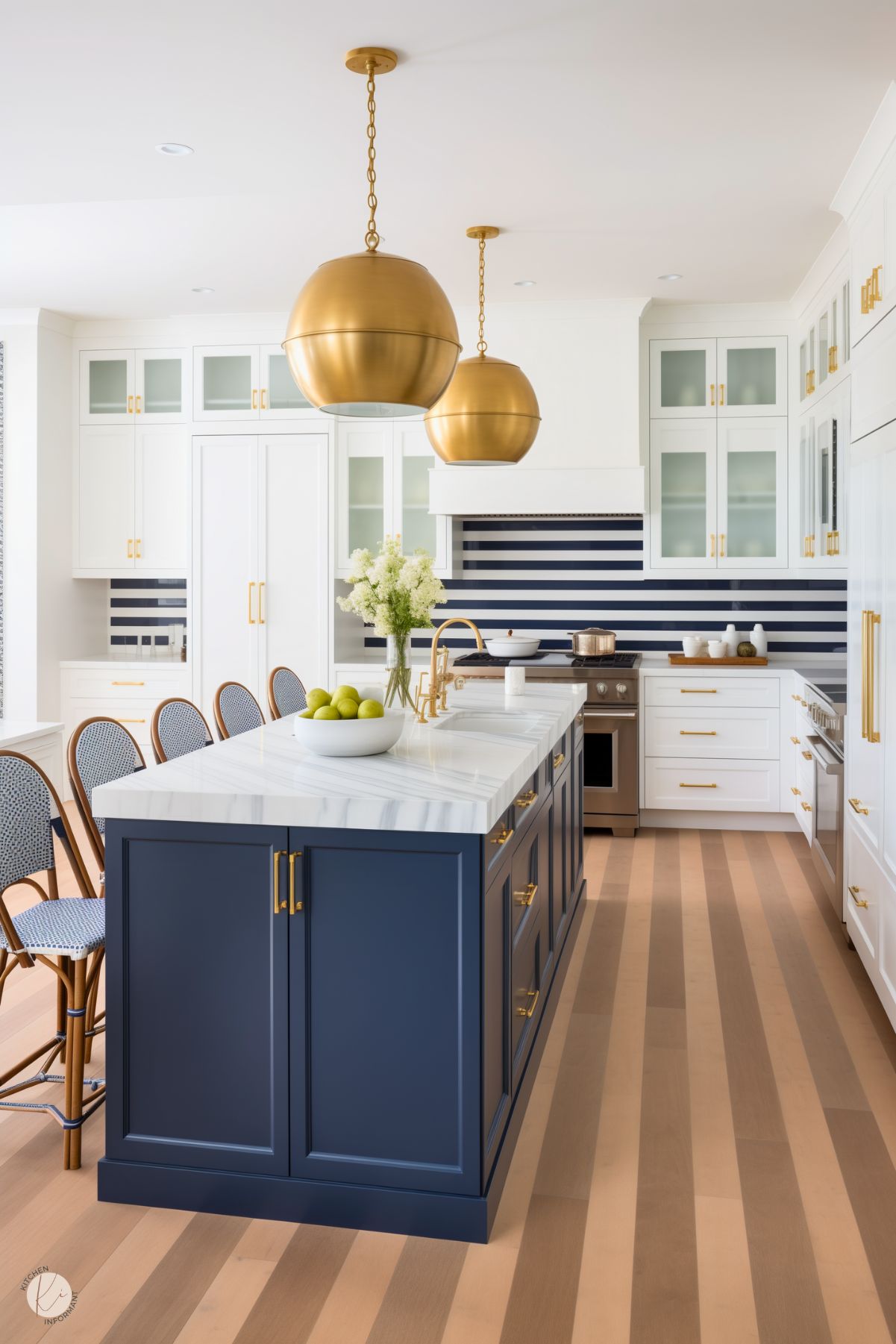 A stylish preppy kitchen with a navy island, white cabinetry, and bold gold hardware. The navy striped backsplash adds a playful touch, while oversized gold pendant lights and rattan-backed barstools enhance the modern, elegant design.