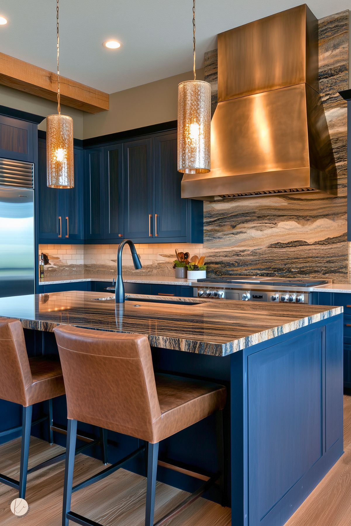 A contemporary kitchen featuring bold navy-blue cabinetry paired with warm copper hardware. The centerpiece is a striking island with a textured stone countertop and integrated sink, complemented by brown leather bar stools. A dramatic copper range hood sits above a marbled backsplash with flowing patterns that match the island. Overhead, two metallic pendant lights provide warm illumination, while the stainless steel refrigerator and wood accents add a balanced mix of modern and rustic elements.