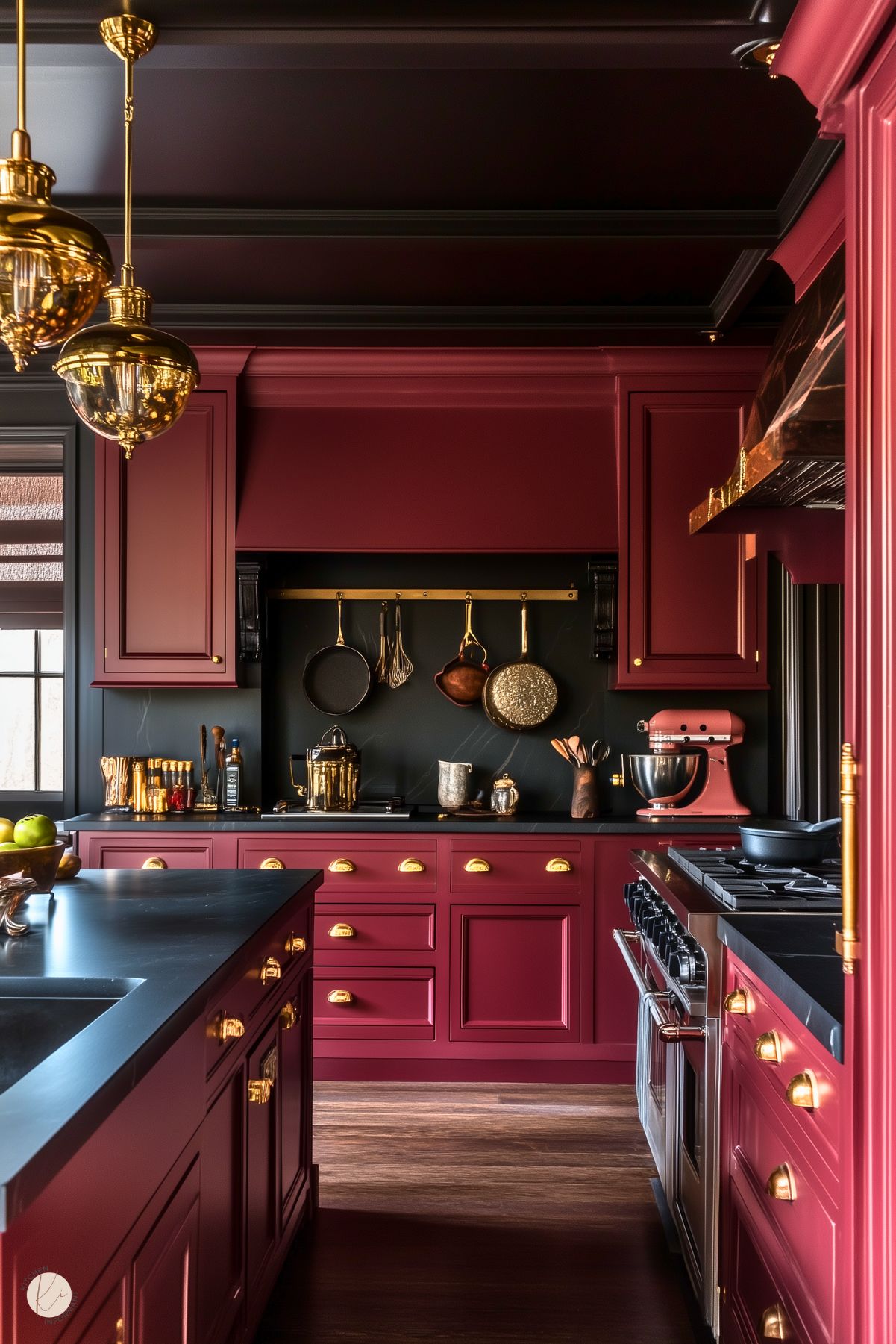 A bold kitchen design featuring deep burgundy cabinetry with gold hardware and accents. The dark countertops and backsplash provide a striking contrast, while open shelving showcases copper and brass cookware. Overhead, gold pendant lights illuminate the space, adding warmth and elegance. A stainless steel stove and a matching burgundy stand mixer complete the luxurious yet functional look.