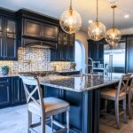 A kitchen with navy blue cabinets, brass hardware, and a granite island. Globe pendant lights add warmth, while a mosaic tile backsplash adds texture. Upholstered barstools and stainless steel appliances complete the look.