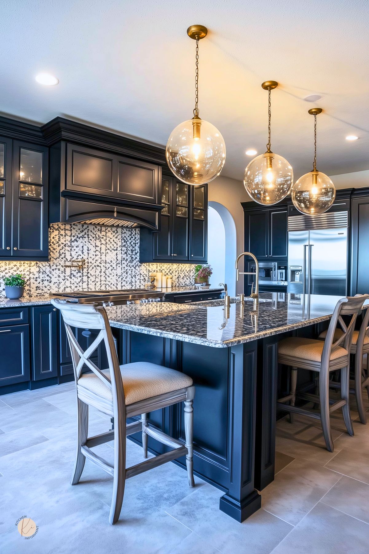 A kitchen with navy blue cabinets, brass hardware, and a granite island. Globe pendant lights add warmth, while a mosaic tile backsplash adds texture. Upholstered barstools and stainless steel appliances complete the look.