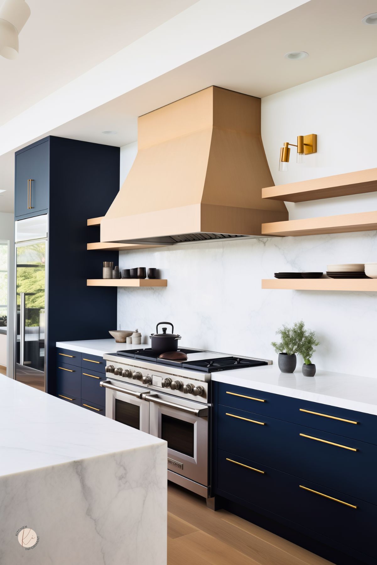 A modern kitchen with navy blue cabinetry, gold hardware, and a statement wood range hood. Floating natural wood shelves contrast against a sleek white marble backsplash, while a high-end stainless steel stove adds a professional touch. A large waterfall marble island complements the space, and gold wall sconces provide warm, elegant lighting. Light wood flooring enhances the bright, airy feel.