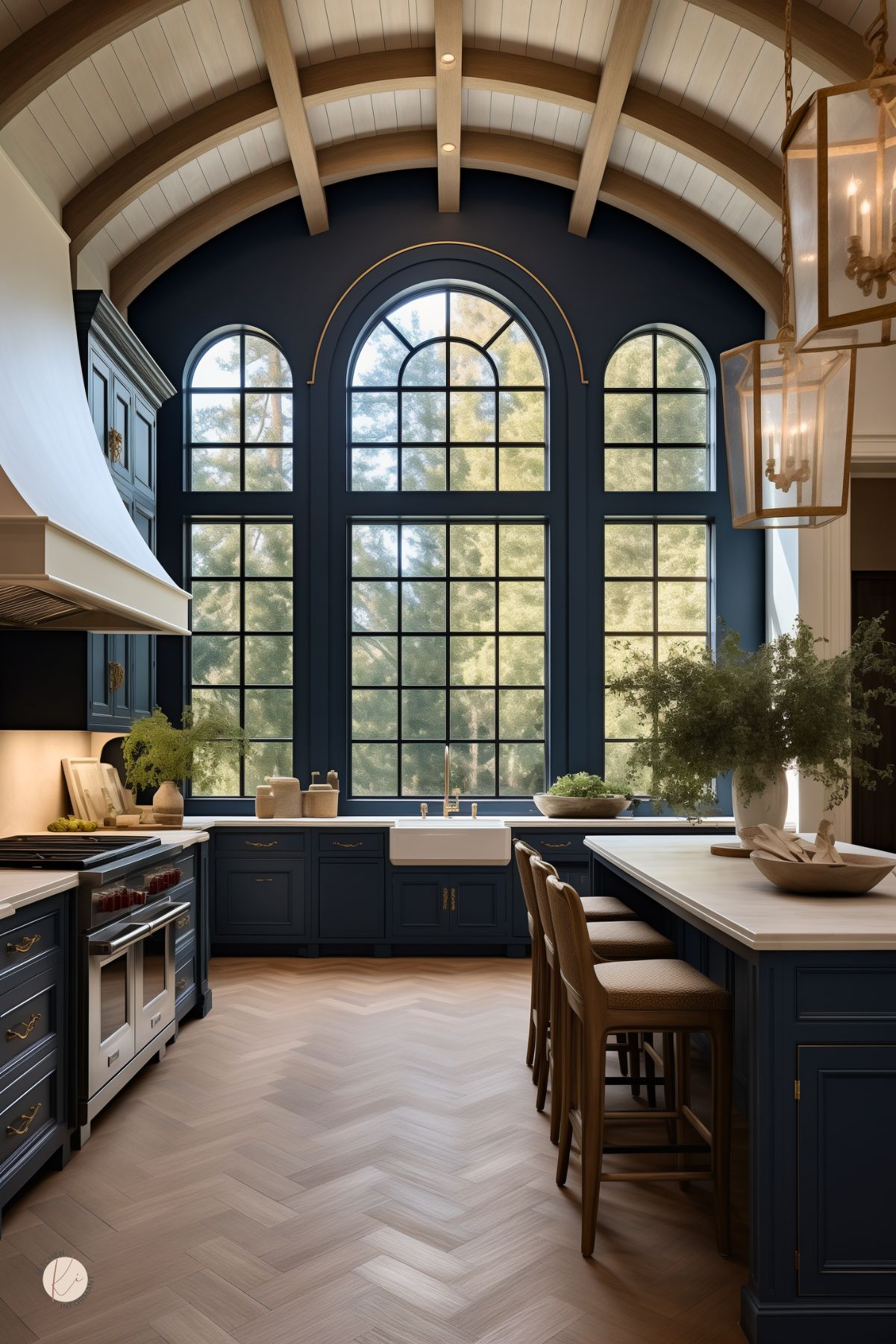 A grand kitchen with navy blue cabinetry, arched black-framed windows, and a vaulted ceiling with exposed wood beams. A large farmhouse sink is set beneath the windows, bringing in natural light. The space features a white marble island with wood barstools, brass hardware, and elegant lantern-style pendant lights. Herringbone wood flooring adds warmth to the sophisticated design.