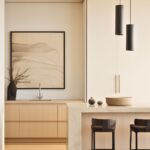 A minimalist cream kitchen with sleek cabinetry, a stone island, and black barstools. Black pendant lights and abstract artwork add contrast, while natural wood tones create warmth.