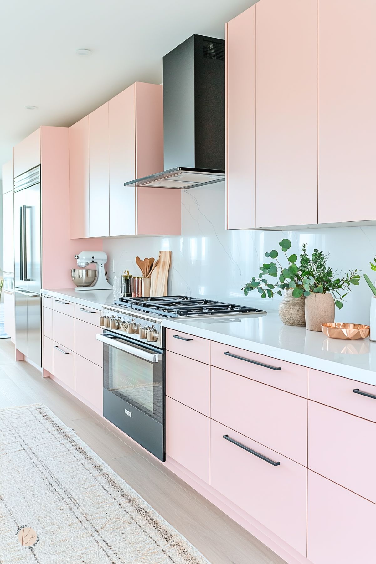 Sleek modern kitchen with flat-front pastel pink cabinets, white quartz countertops, and a black range hood for bold contrast. Minimalist black handles add a contemporary edge, while soft wood floors and greenery in ceramic planters bring warmth and freshness. A white marble-style backsplash and light-toned rug complete the airy, Scandinavian-inspired space.