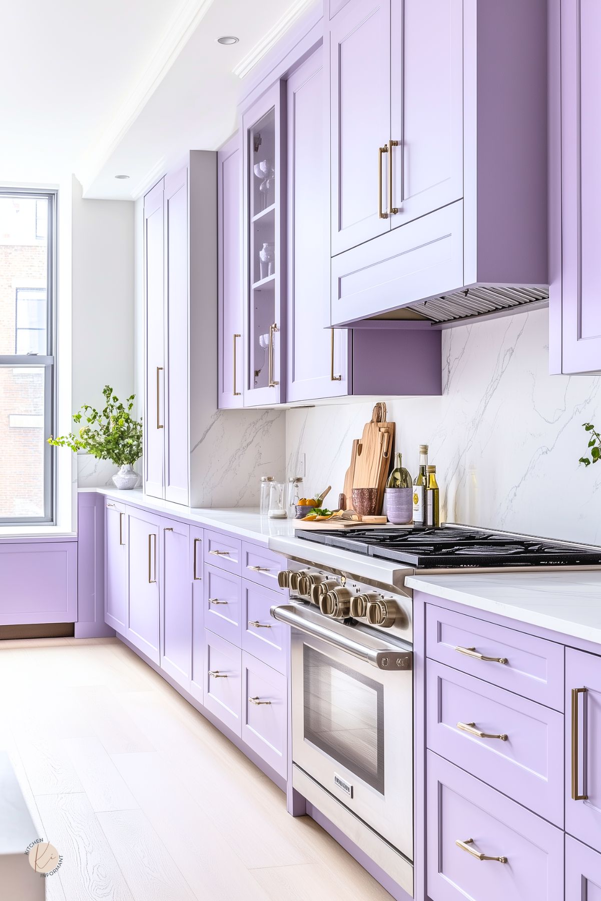 Contemporary lavender kitchen with shaker cabinets, sleek gold hardware, and white quartz countertops. The backsplash features subtle marble veining, complementing the light wood floors. Stainless steel range and vent add a modern touch, while wood cutting boards and fresh greenery soften the look. Large window brings in natural light, enhancing the airy feel.