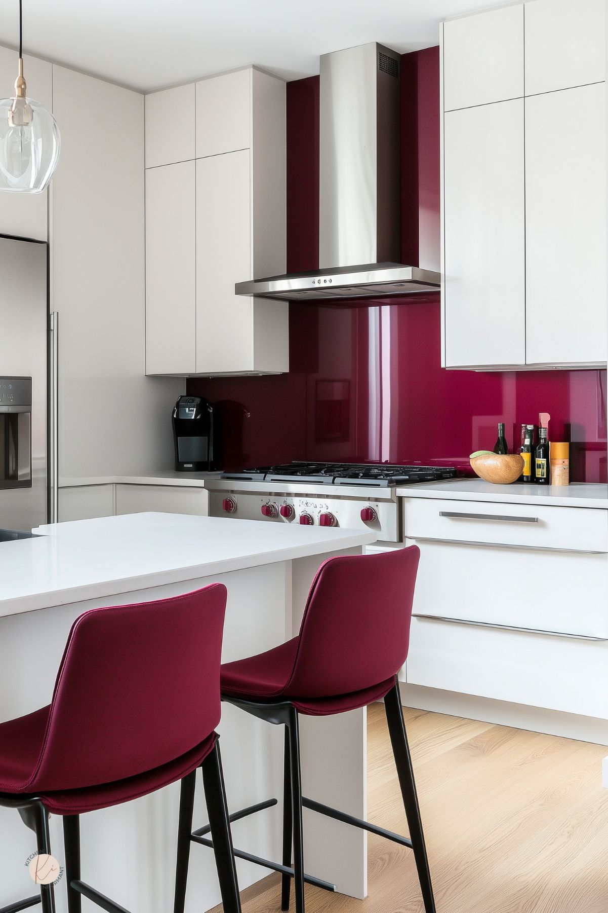 Modern white kitchen with burgundy accents: glossy burgundy glass backsplash, matching bar-stool seats, and burgundy range knobs. Flat-panel cabinets, quartz waterfall island, stainless range and hood, built-in fridge, pendant light, and light wood floors. Minimalist modern kitchen design.